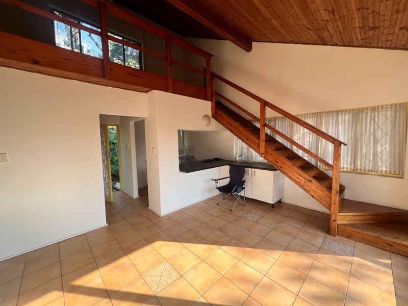 Open plan living area featuring a timber staircase, mezzanine level, vaulted timber ceiling, and a compact kitchen with built-in cabinetry and cooktop.