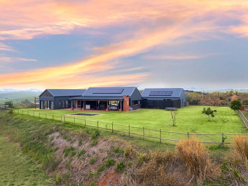 Aerial view of a modern farmhouse-style residence featuring a metal roof with solar panels, a covered patio, swimming pool, and expansive landscaped grounds.