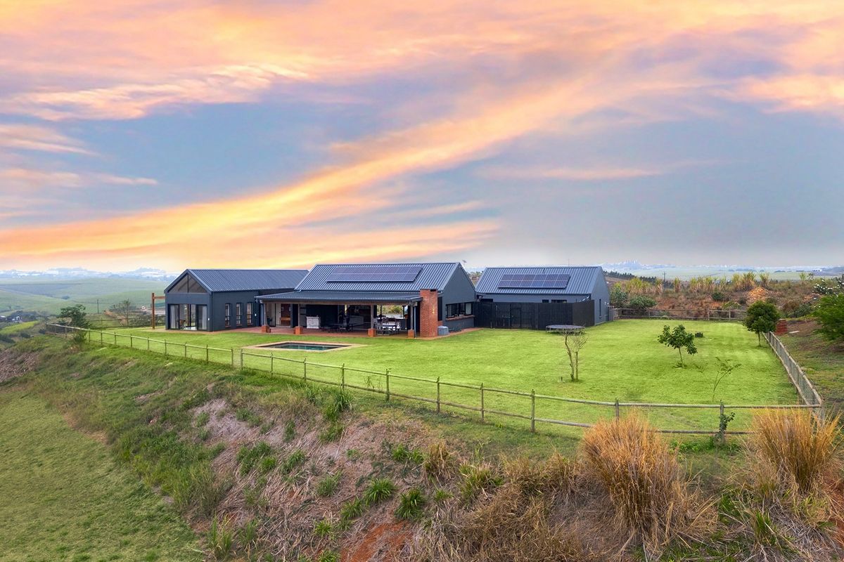 Aerial view of a modern farmhouse-style residence featuring a metal roof with solar panels, a covered patio, swimming pool, and expansive landscaped grounds.