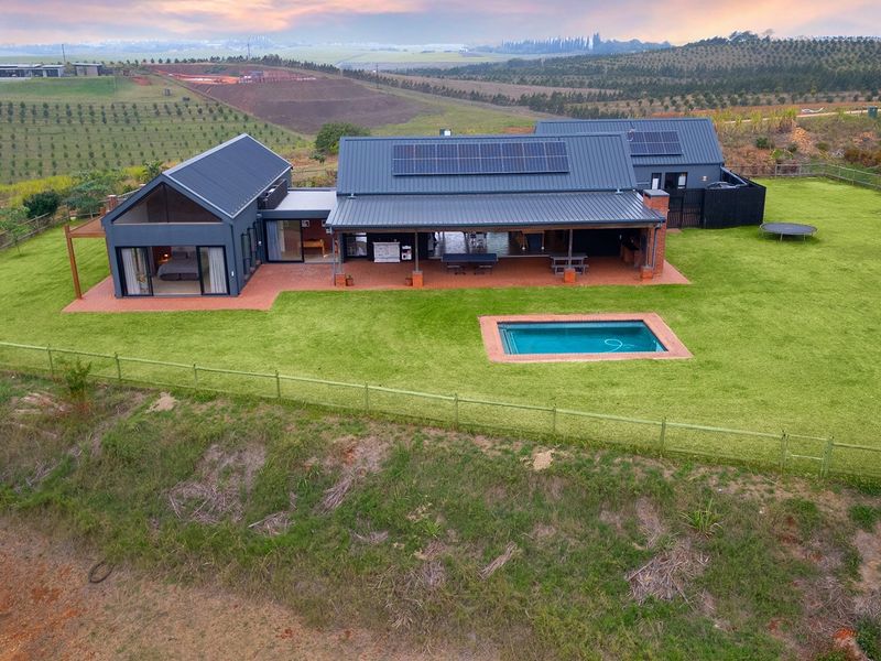 Aerial view of a modern farmhouse-style residence featuring a metal roof, solar panels, a swimming pool, and a spacious covered patio set in a rural landscape.