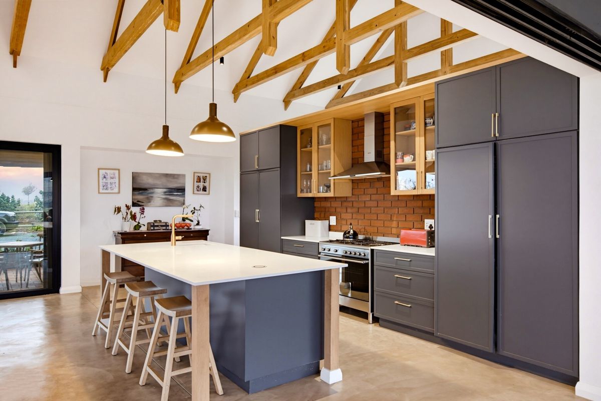Modern kitchen featuring exposed timber trusses, a central island, dark cabinetry, brick splashback, and high-end built-in appliances with polished concrete floors.