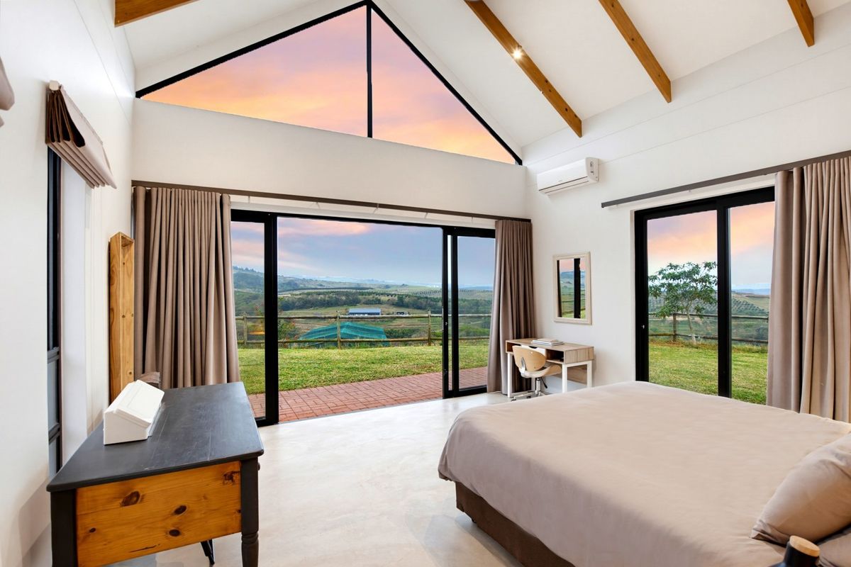 Spacious bedroom featuring a vaulted ceiling with exposed timber beams, large gable window, polished concrete floors, and sliding doors opening to a scenic landscape.