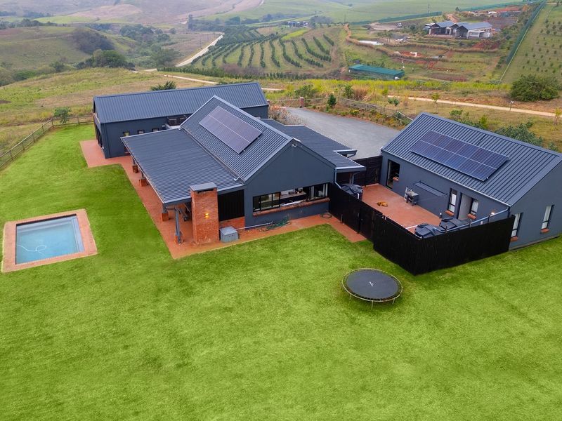 Aerial view of a modern farmhouse-style property featuring a metal roof with solar panels, a swimming pool, and expansive landscaped grounds.