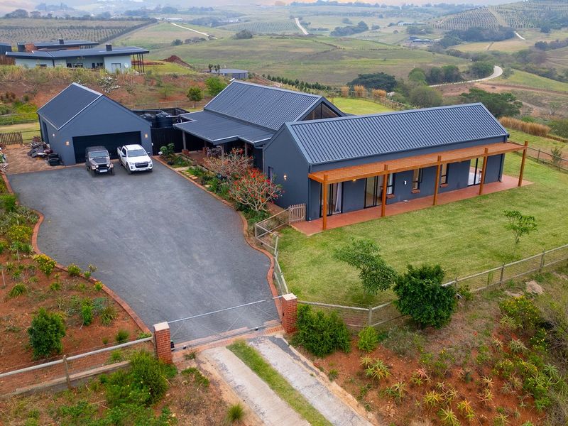 Aerial view of a modern farmhouse with a metal roof, timber pergola, and double garage, set on a spacious rural property with scenic landscape views.