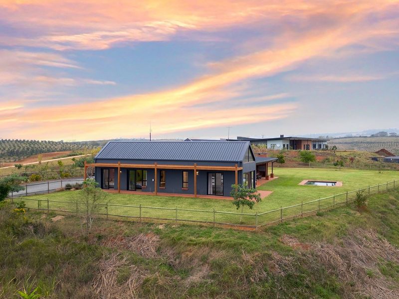 Aerial view of a modern single-story home featuring a metal roof, timber pergola, and a private swimming pool set within a spacious landscaped garden.