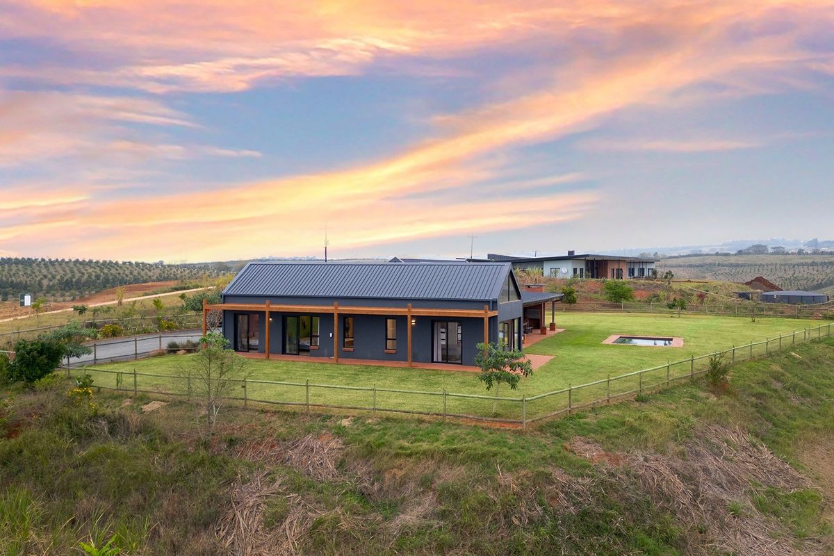 Aerial view of a modern single-story home featuring a metal roof, timber pergola, and a private swimming pool set within a spacious landscaped garden.
