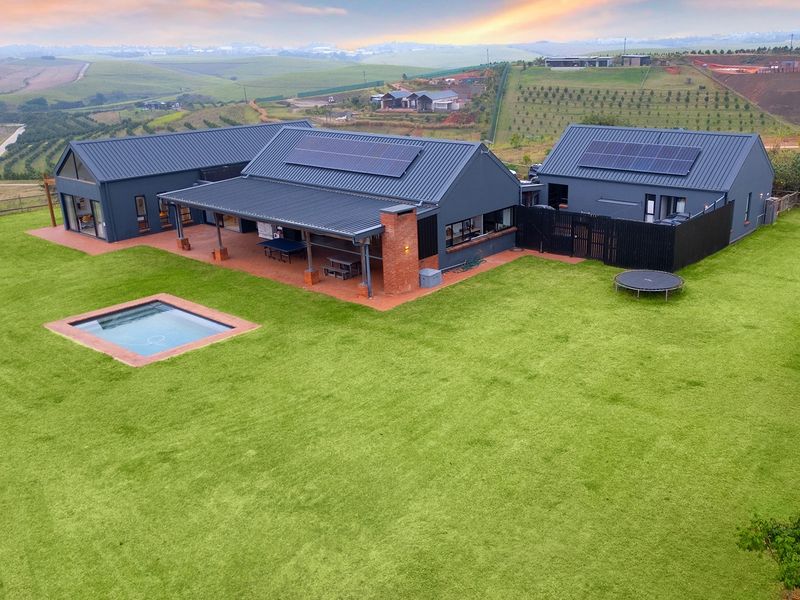 Aerial view of a modern farmhouse-style property featuring a metal roof with solar panels, a swimming pool, and a spacious covered patio.