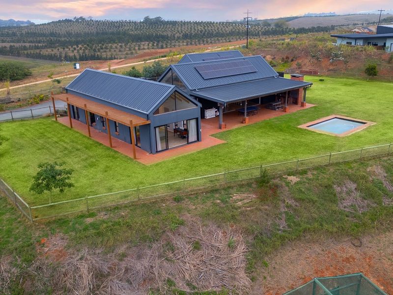 Aerial view of a modern farmhouse-style residence featuring a metal roof with solar panels, expansive covered patio, and a private swimming pool.