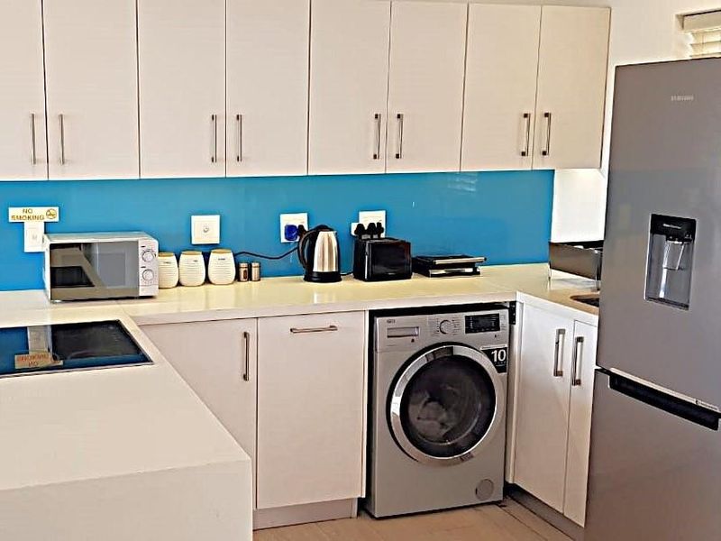 Modern kitchen featuring white cabinetry, stone countertops, a vibrant blue glass splashback, and an integrated washing machine.