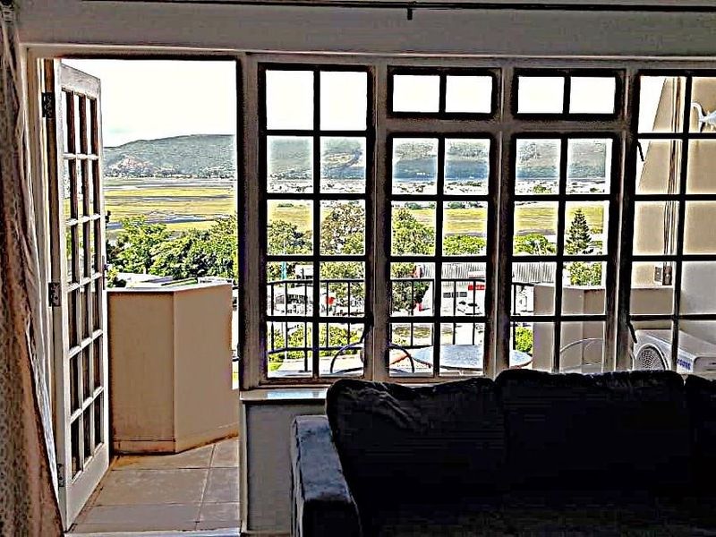 Living room featuring large grid-pattern windows and french doors opening onto a balcony with scenic landscape views.