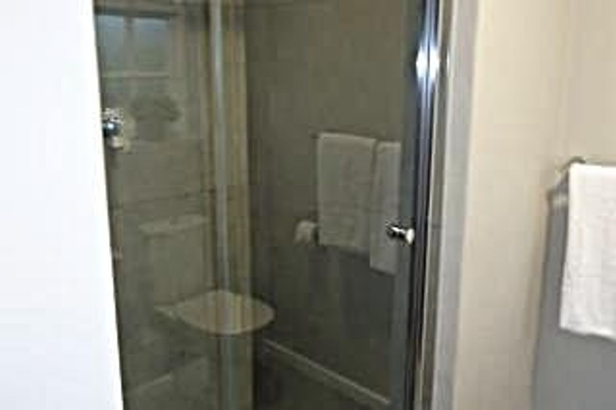 A compact bathroom featuring a glass-enclosed shower and a standard toilet with neutral wall tiling.