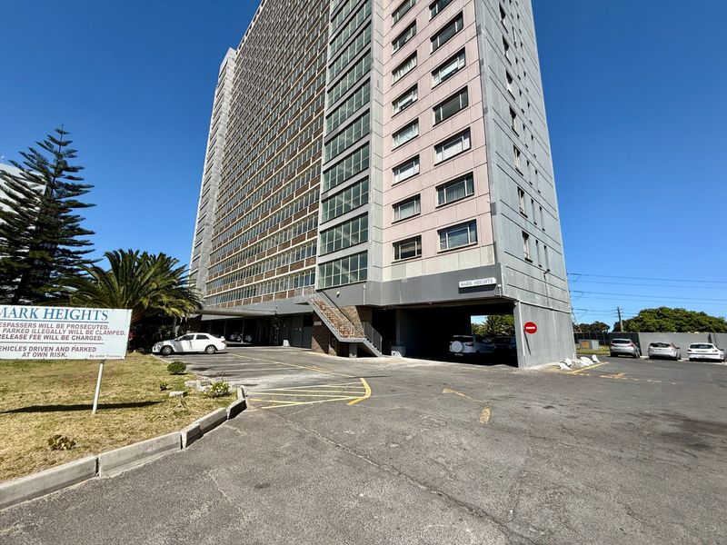 Exterior view of Mark Heights apartment building featuring a large concrete facade, covered parking area, and asphalt driveway access.