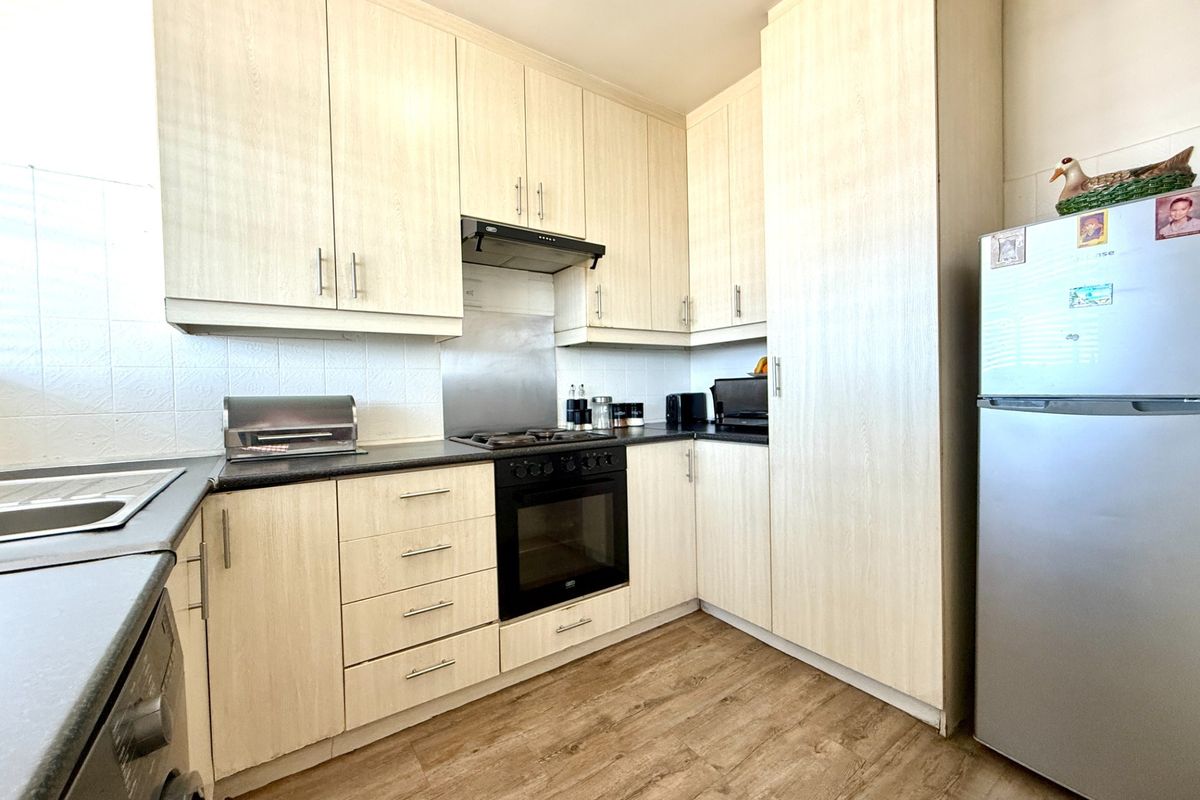 A functional kitchen featuring light wood-grain cabinetry, dark countertops, integrated oven and hob, and durable laminate flooring.