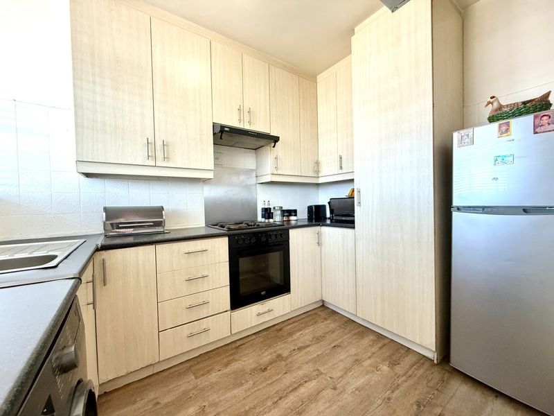 A functional kitchen featuring light wood-grain cabinetry, dark countertops, integrated oven and hob, and durable laminate flooring.