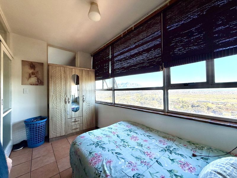 A bedroom featuring tiled flooring, large windows with bamboo blinds, and expansive views, providing a bright and functional living space.