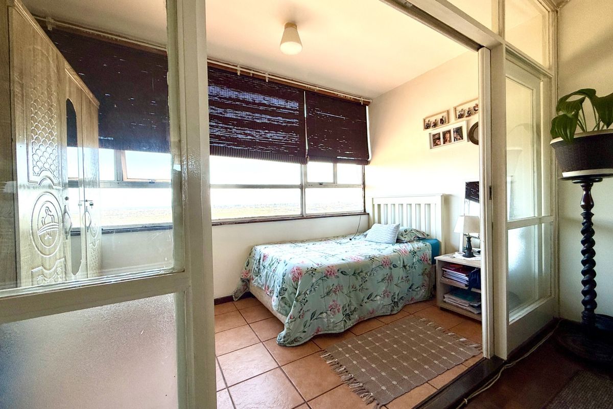 A bedroom featuring terracotta floor tiles and a large window, accessed via a sliding glass partition door.