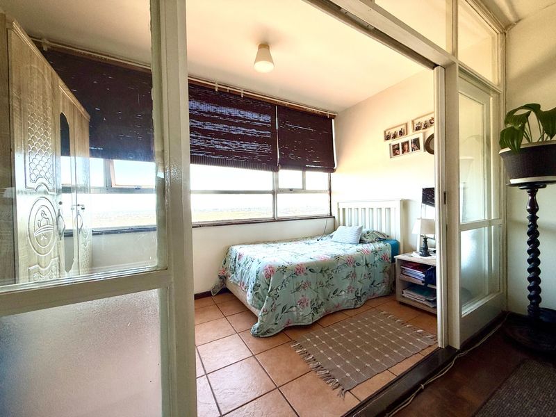 A bedroom featuring terracotta floor tiles and a large window, accessed via a sliding glass partition door.