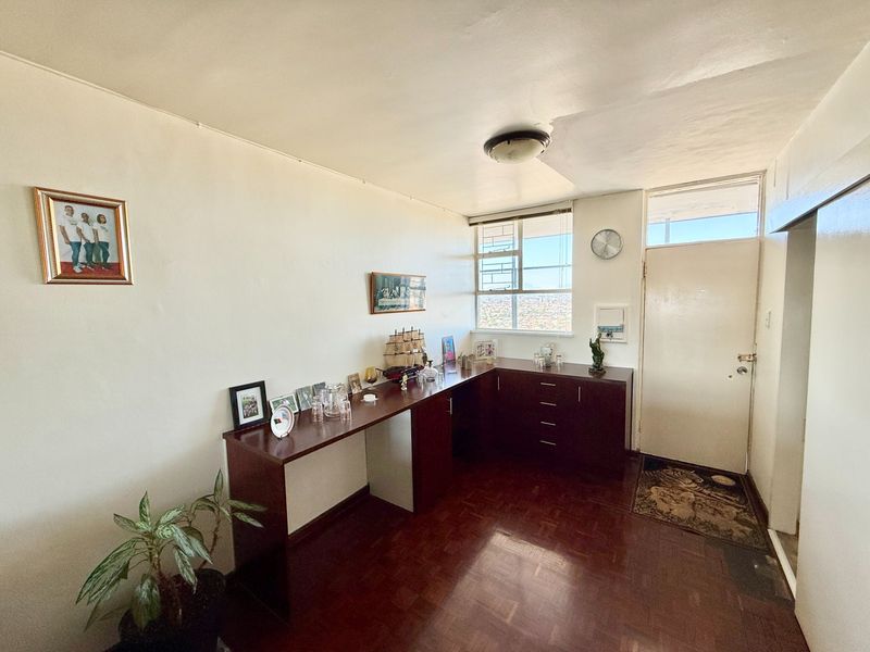 A living area featuring dark wood parquet flooring, built-in cabinetry, and a large window with city views. The space requires cosmetic updates to the ceiling.
