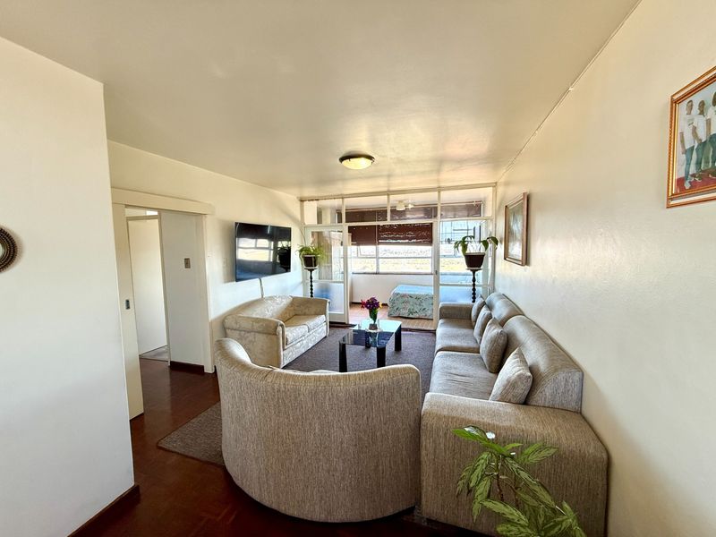 A spacious living room featuring hardwood flooring and a large sliding glass door leading to an enclosed balcony area.