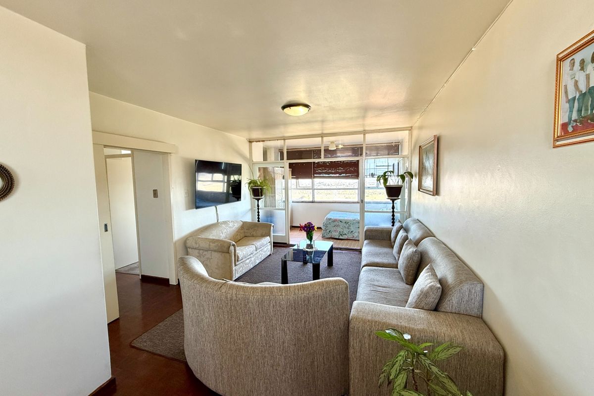 A spacious living room featuring hardwood flooring and a large sliding glass door leading to an enclosed balcony area.