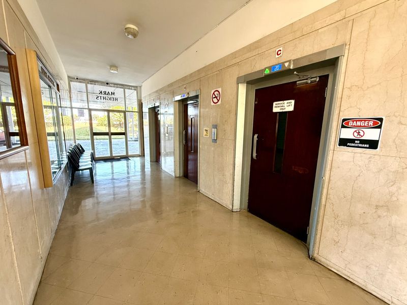 A clean apartment building lobby featuring marble wall finishes, tiled flooring, and multiple elevator access points.