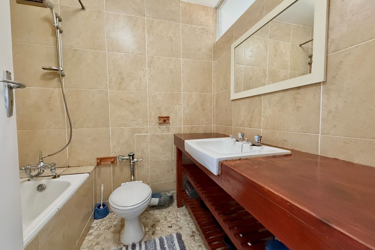 A functional bathroom featuring a bathtub with shower mixer, a toilet, and a wooden vanity with a basin, finished with neutral wall tiles.
