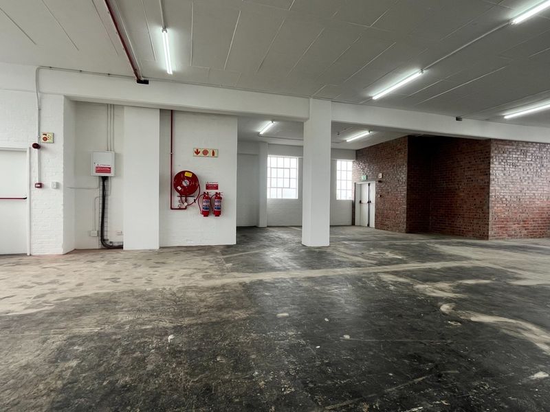 Spacious industrial utility area featuring exposed brickwork, concrete flooring, fire safety equipment, and ample natural light from large windows.