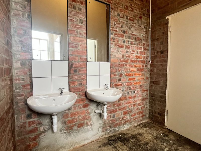 Industrial-style bathroom featuring exposed brick walls, dual wall-mounted basins with chrome fixtures, and simple mirrors, offering a raw, functional aesthetic.
