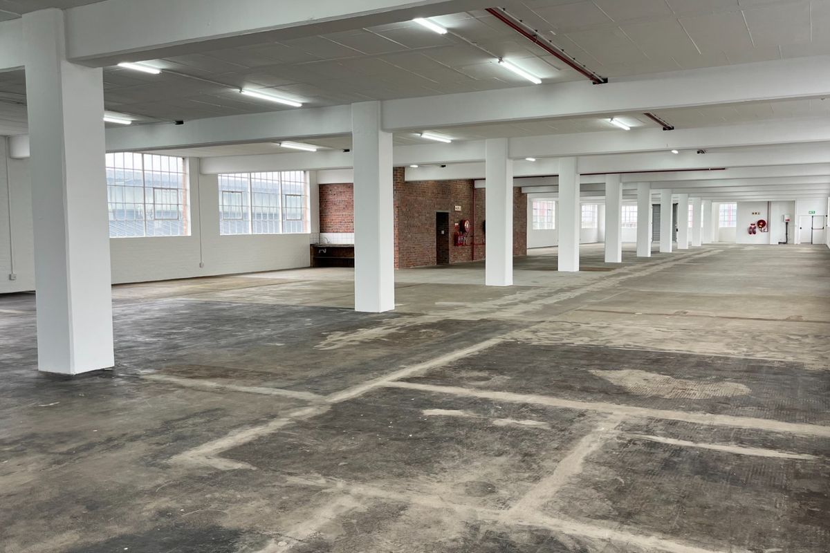 Expansive open-plan industrial warehouse space featuring high ceilings, exposed concrete columns, large industrial windows, and durable concrete flooring throughout.