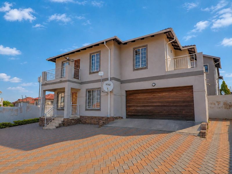 Front exterior view of a double-story house featuring a paved driveway, double garage, and upper-level balcony with security fencing.