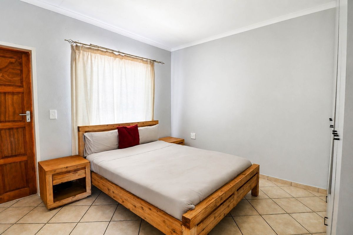 A functional bedroom featuring tiled flooring, neutral wall finishes, and a built-in wardrobe, providing a clean and simple living space.