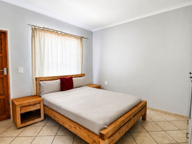 A functional bedroom featuring tiled flooring, neutral wall finishes, and a built-in wardrobe, providing a clean and simple living space.