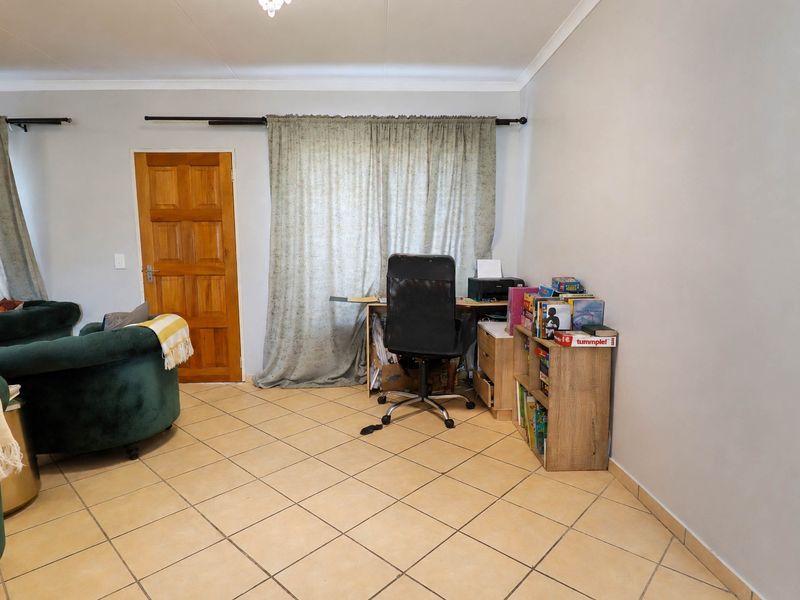 A living area featuring neutral tiled flooring, a timber door, and coved ceilings, providing a functional space for relaxation or home office use.