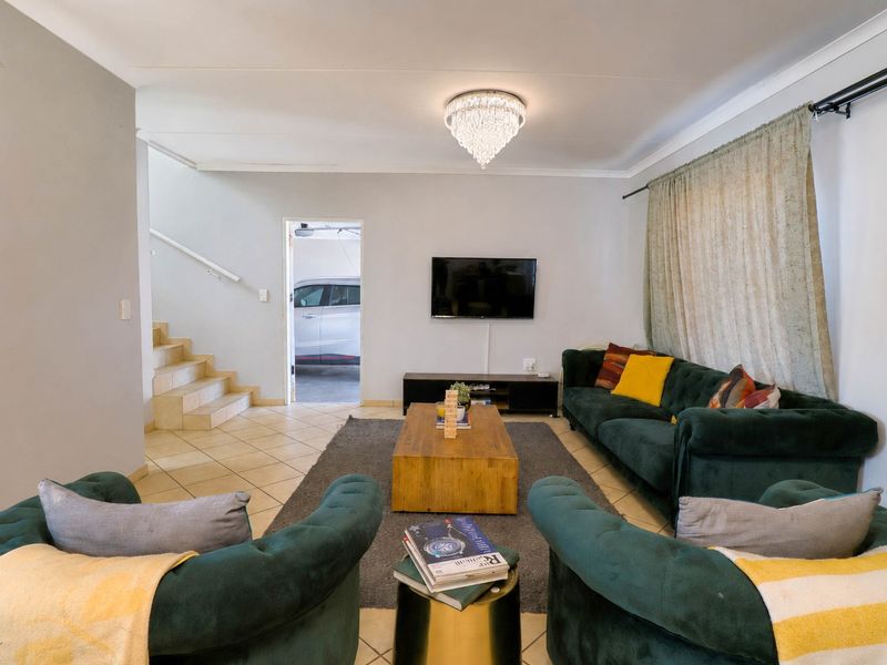 A comfortable living room featuring tiled flooring, a central crystal chandelier, and direct access to the garage area via an internal staircase.