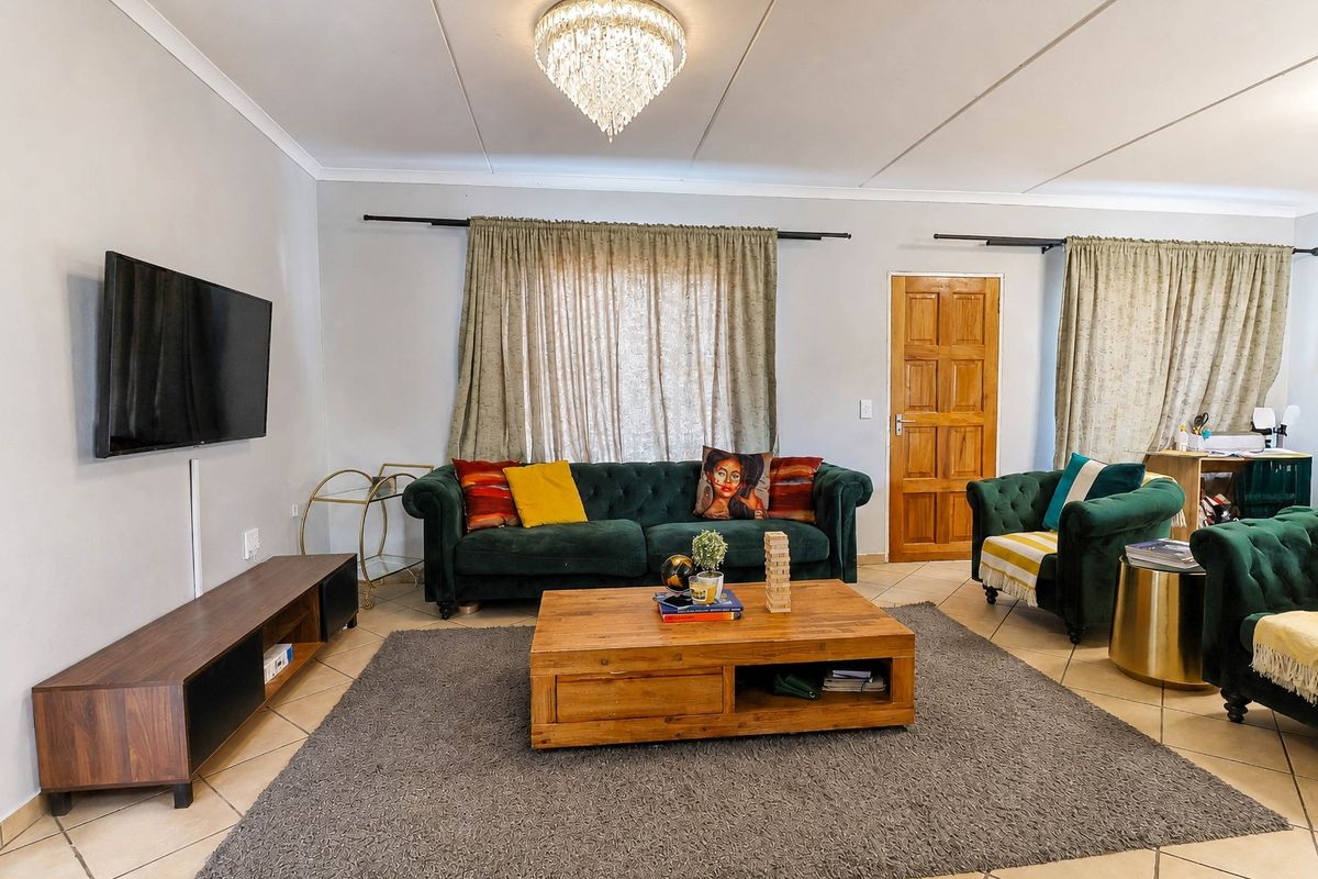 A comfortable living room featuring tiled flooring, a central crystal chandelier, and a classic timber panel door.