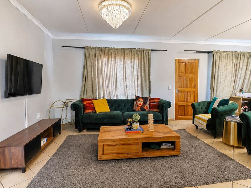 A comfortable living room featuring tiled flooring, a central crystal chandelier, and a classic timber panel door.