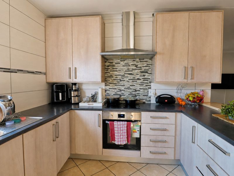 A well-maintained kitchen featuring light wood-finish cabinetry, dark countertops, a mosaic tile splashback, and integrated stainless steel appliances.