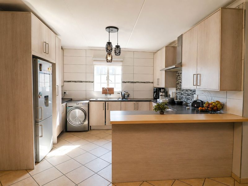 A well-maintained kitchen featuring light wood-finish cabinetry, tiled backsplash, integrated appliances, and a breakfast bar counter with ceramic floor tiles.