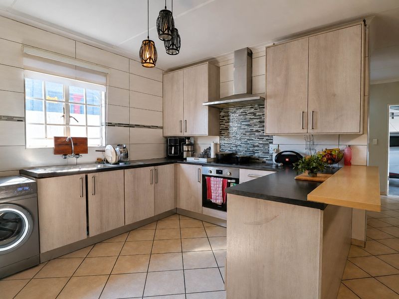Modern kitchen featuring light wood-finish cabinetry, dark countertops, a breakfast bar, stainless steel appliances, and a tiled backsplash.