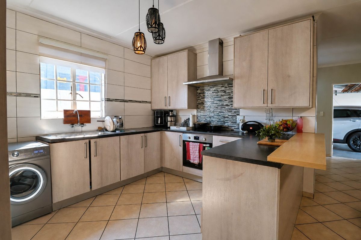Modern kitchen featuring light wood-finish cabinetry, dark countertops, a breakfast bar, stainless steel appliances, and a tiled backsplash.
