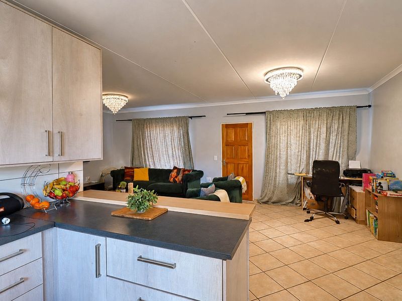 Open-plan living area featuring tiled flooring, light-toned cabinetry, and dual crystal light fixtures, creating a functional combined kitchen and living space.