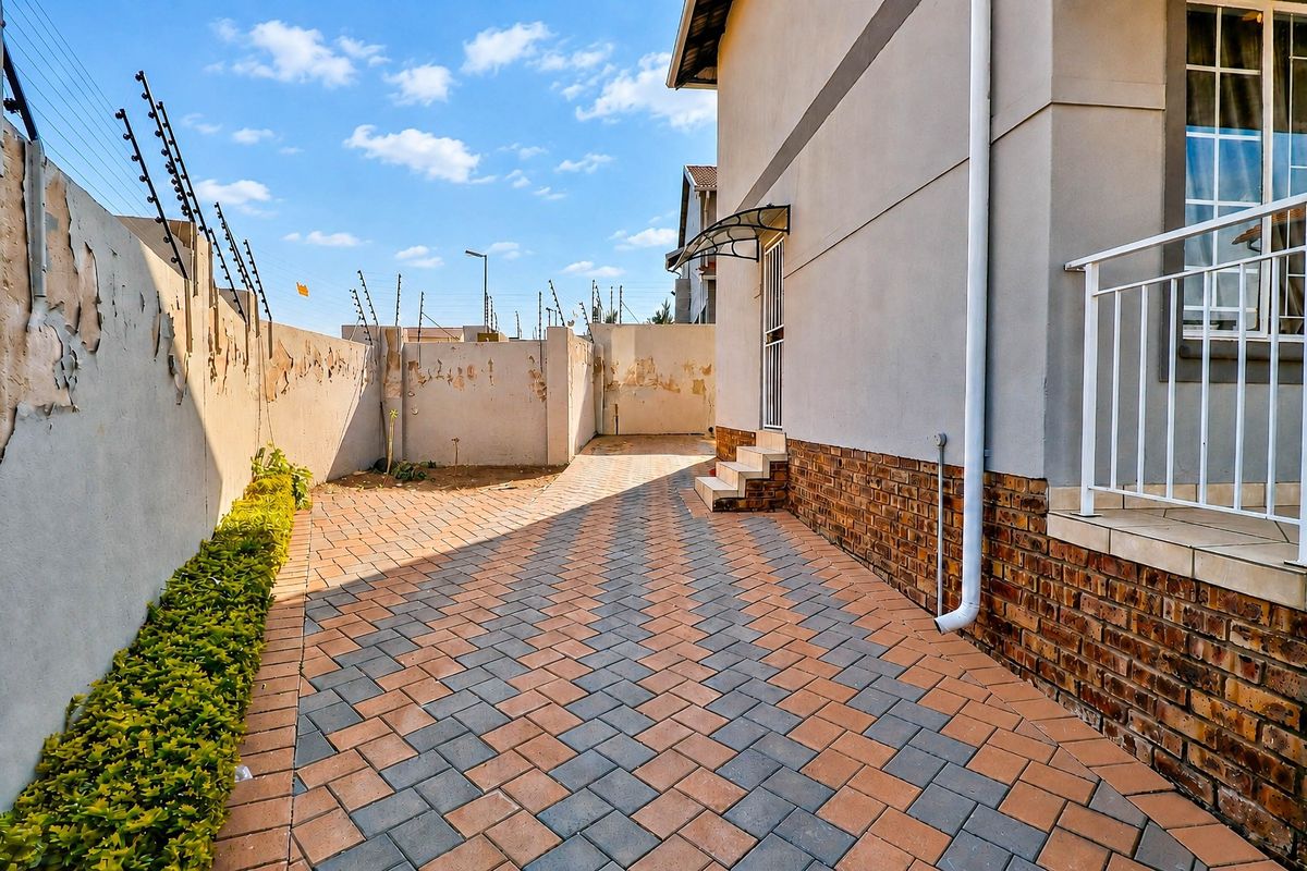 A paved side yard area featuring a brick-accented building facade, security gate, and perimeter boundary walls with electric fencing.