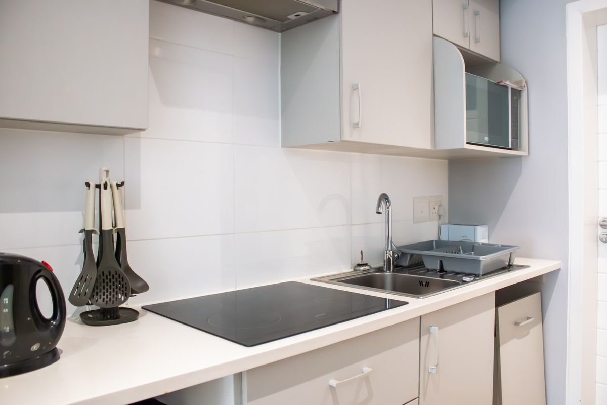 A compact, modern kitchen featuring light-toned cabinetry, a sleek electric hob, integrated extractor fan, and a stainless steel sink with tiled splashback.