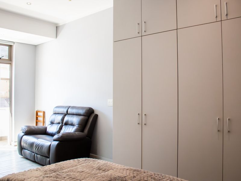 A well-lit bedroom featuring neutral walls, modern built-in cupboards with sleek handles, and a sliding door providing access to an outdoor area.