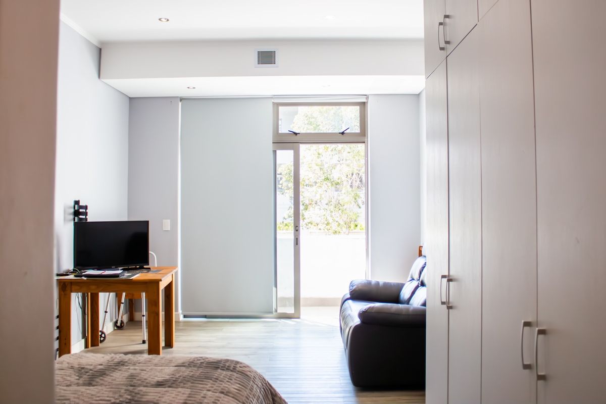 A bright bedroom featuring built-in cupboards, laminate flooring, and a sliding glass door providing access to an outdoor area.