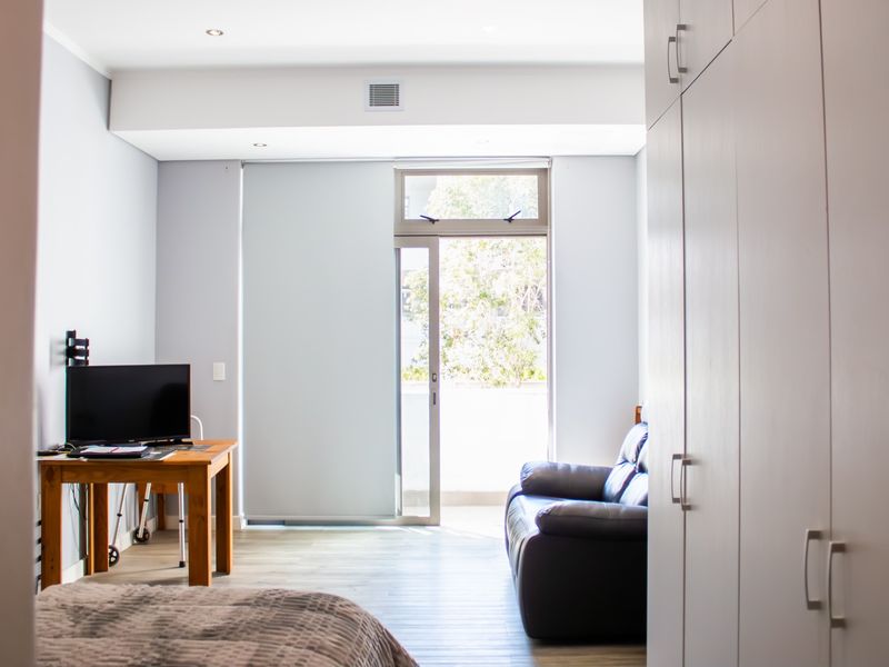 A bright bedroom featuring built-in cupboards, laminate flooring, and a sliding glass door providing access to an outdoor area.