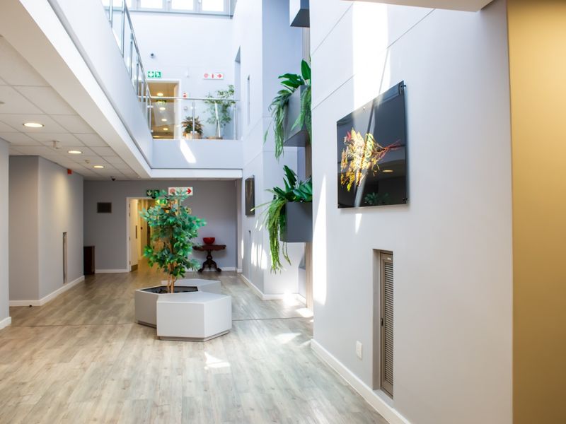 A bright, modern atrium-style hallway featuring high ceilings, laminate flooring, and a glass balustrade overlooking the lower level.