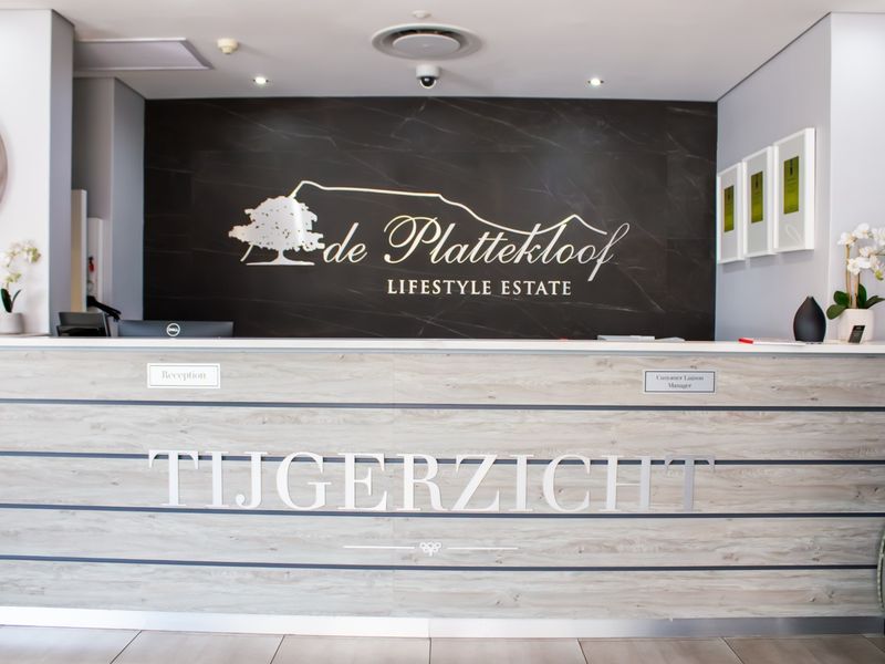 Professional reception area featuring a modern wood-look desk, dark feature wall with estate branding, and clean tiled flooring in a well-maintained retirement village.