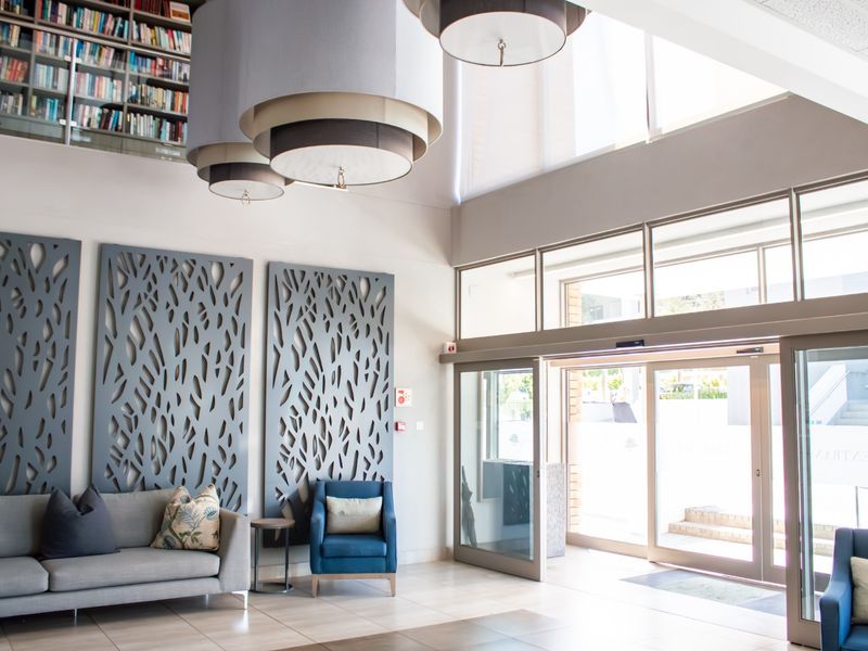 A bright and modern retirement village entrance lobby featuring high ceilings, large pendant lighting, decorative wall panels, and automatic sliding glass doors.
