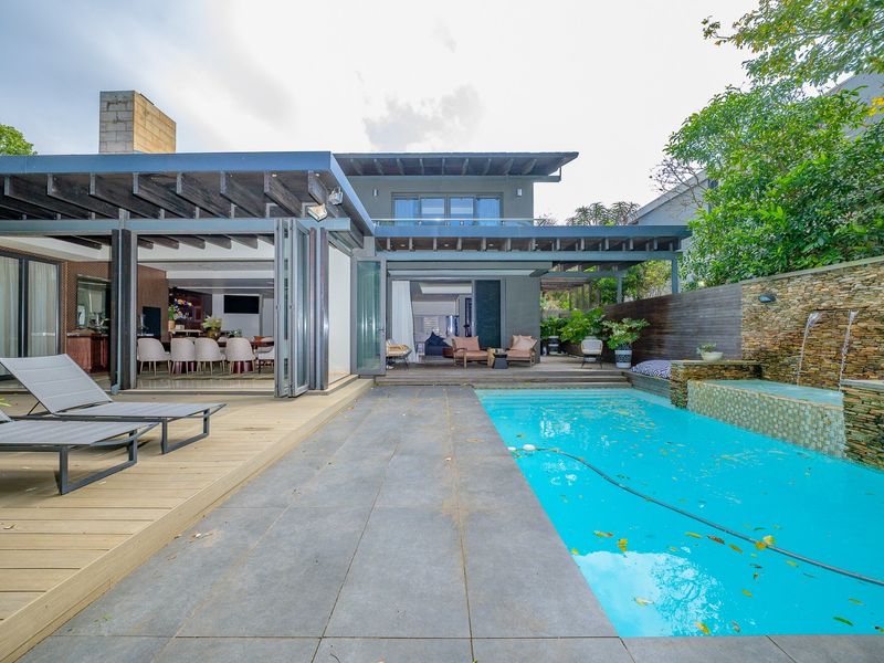 Outdoor entertainment area featuring a swimming pool with a stone water feature, timber decking, and seamless indoor-outdoor flow through stacking glass doors.